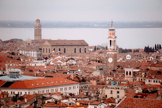 Panoramic aerial view of Venice showcasing red rooftops, towers, and historic architecture under a cloudy sky.