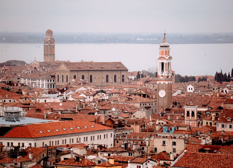 Panoramic aerial view of Venice showcasing red rooftops, towers, and historic architecture under a cloudy sky.
