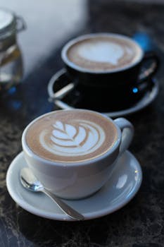 Close-up of beautifully crafted latte art in white and black cups on a marble table.