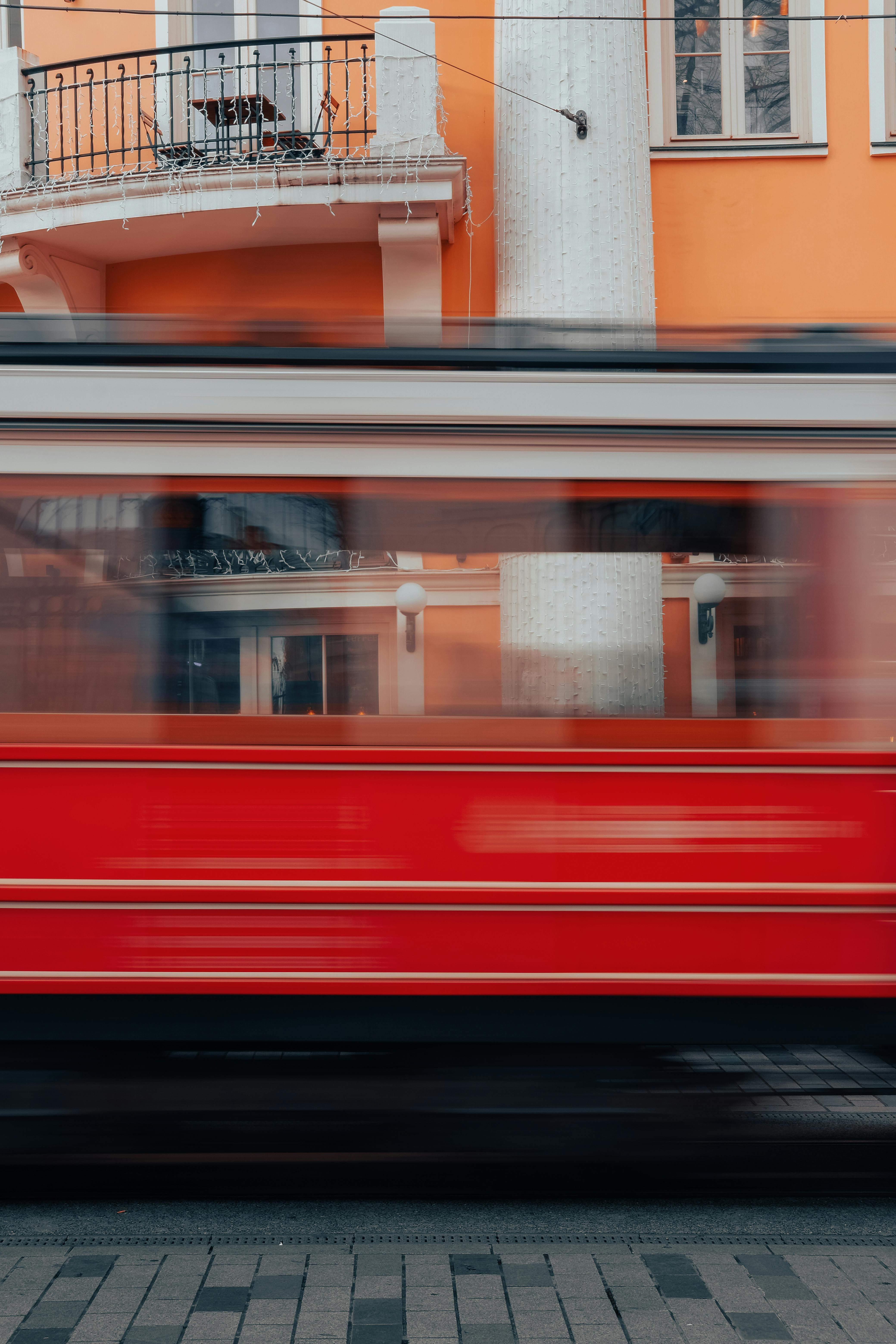 Vibrant red tram captured in a stunning long exposure shot against an orange building backdrop.