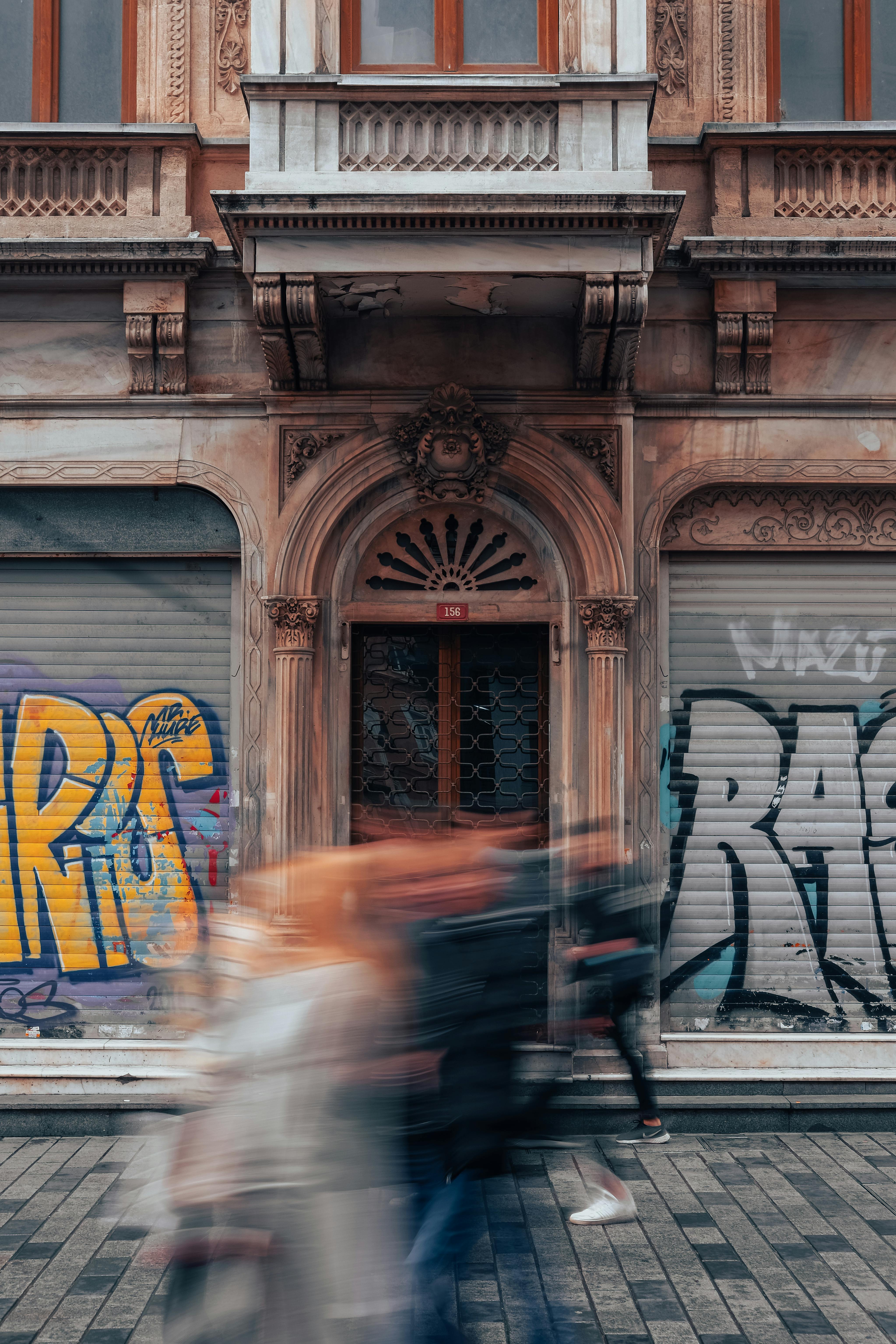 Capture of blurred pedestrians walking past an urban graffiti-adorned building.