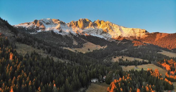 Breathtaking aerial view of snow-covered mountains and pine forests in Lombardy, Italy, during sunset.