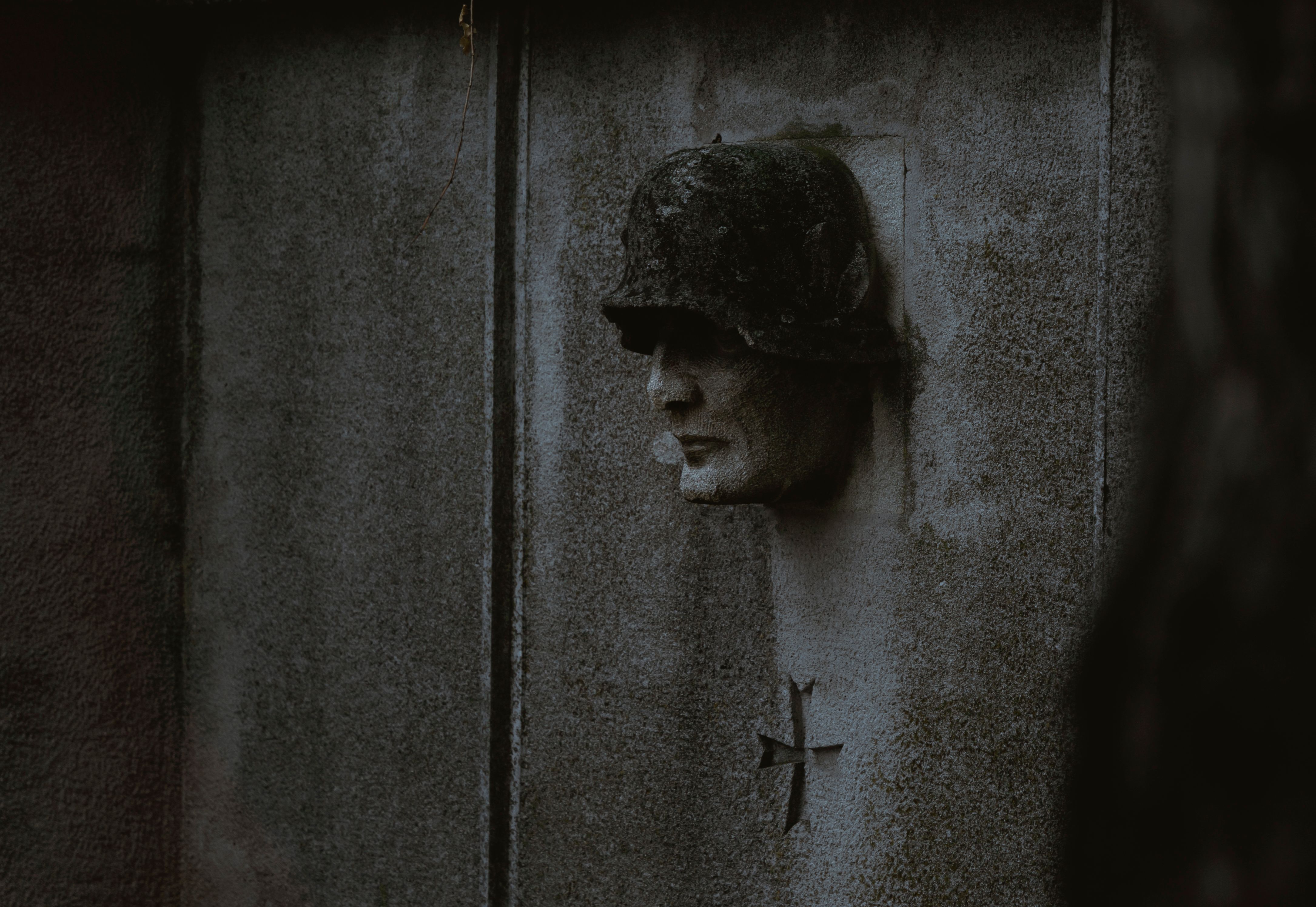 Dark concrete wall with a soldier sculpture and a cross symbol.