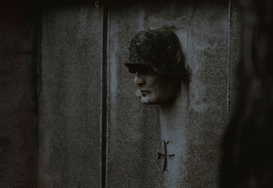 Dark concrete wall with a soldier sculpture and a cross symbol.