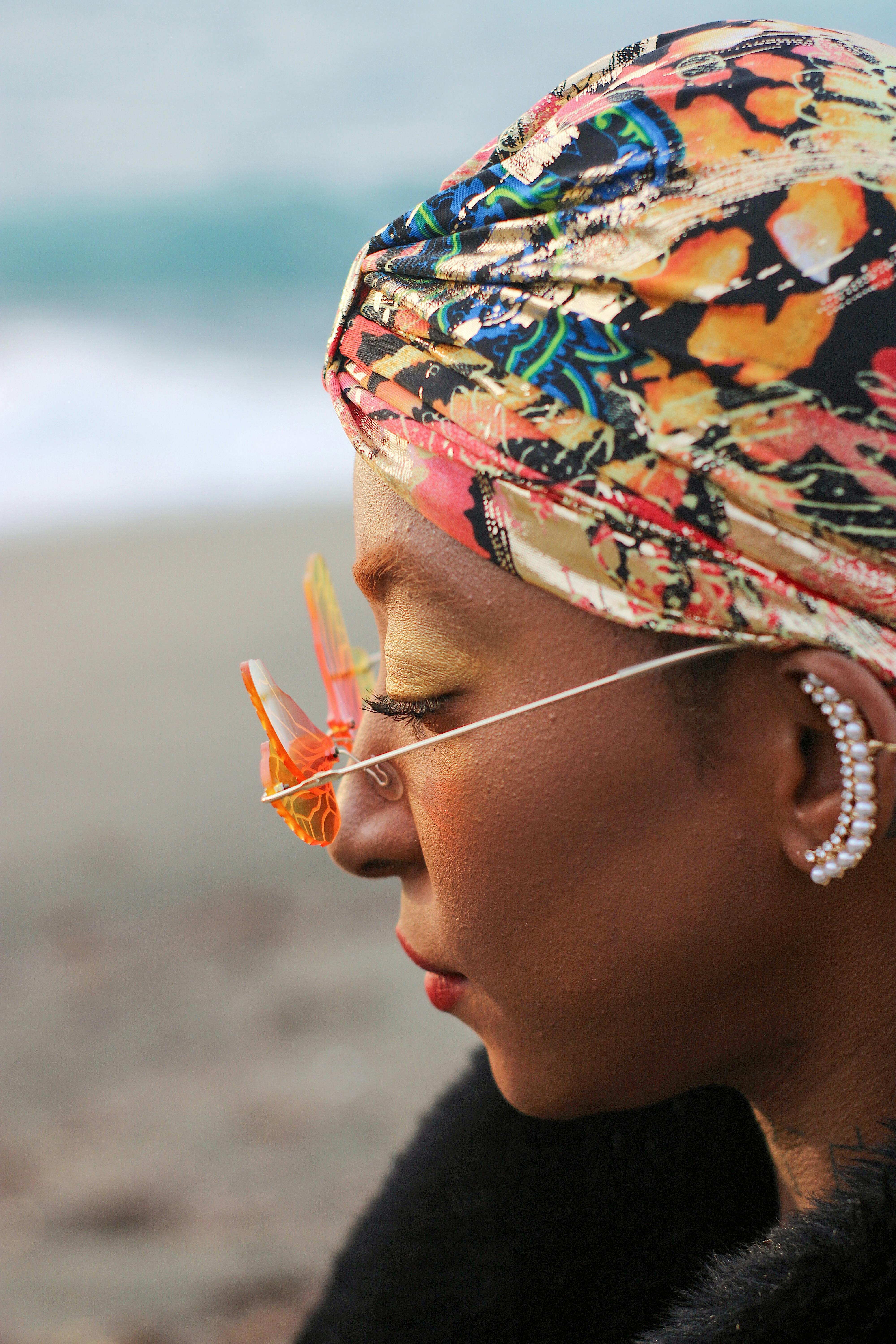 Close-up portrait of a woman with a colorful headscarf and unique sunglasses at the beach.