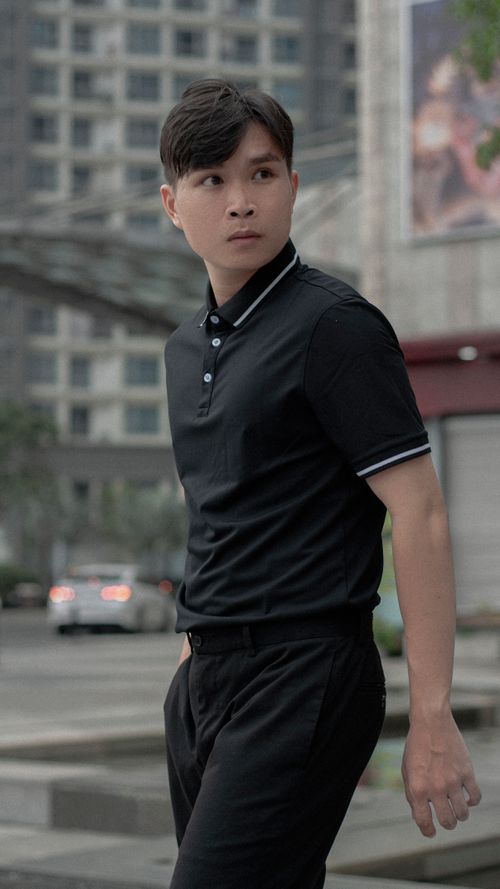 Free Stylish young man in black polo shirt posing confidently on city street. Stock Photo