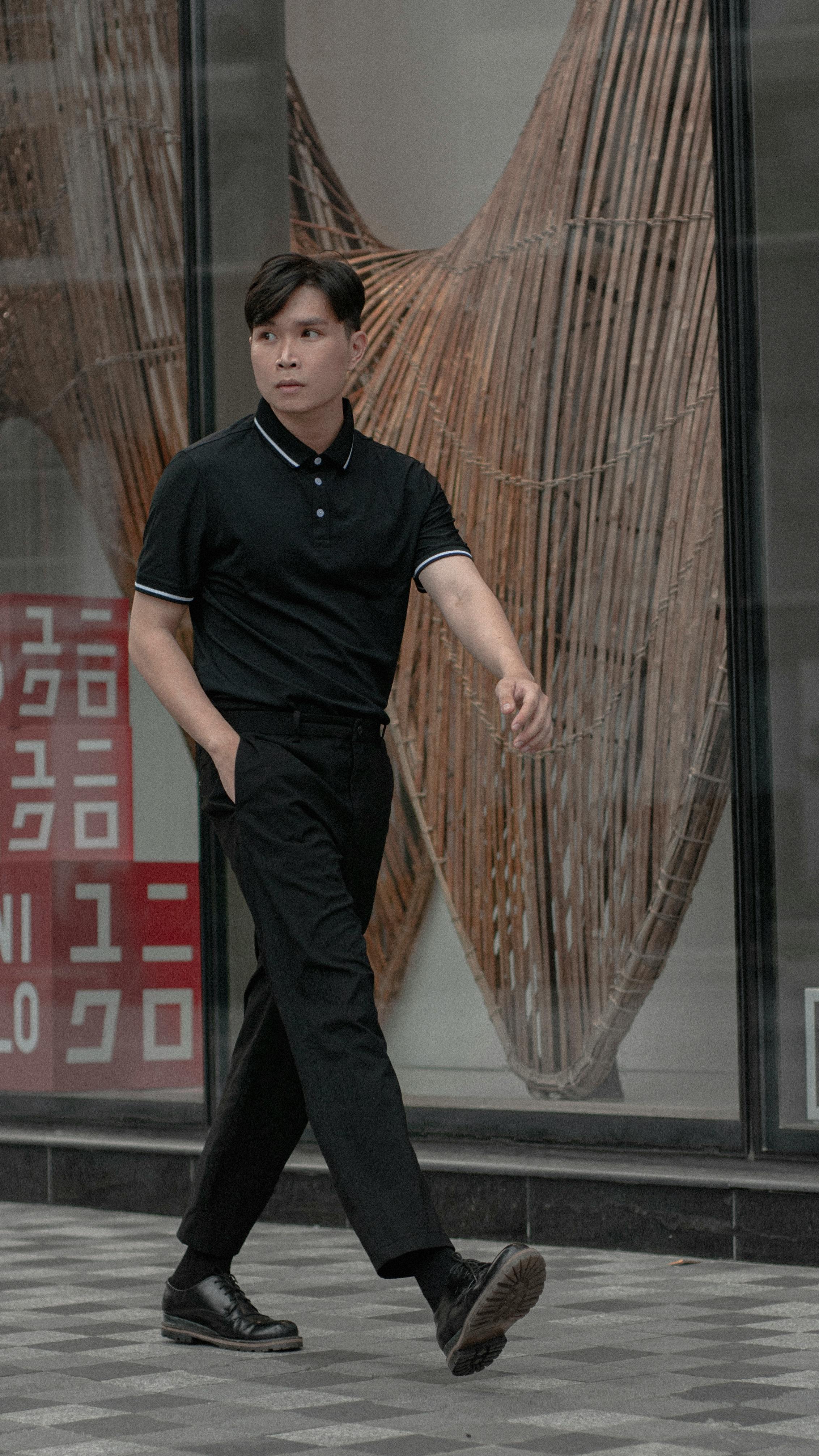 Stylish man in black clothes walking confidently on a city sidewalk with modern background.