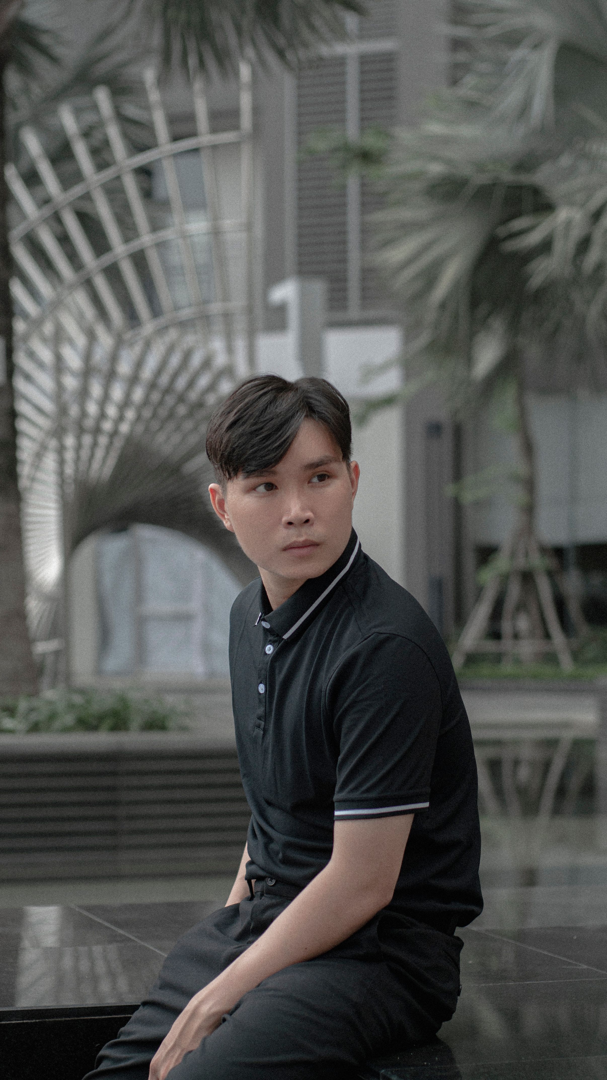 A fashionable man in a polo shirt sits stylishly outdoors in a modern urban environment.