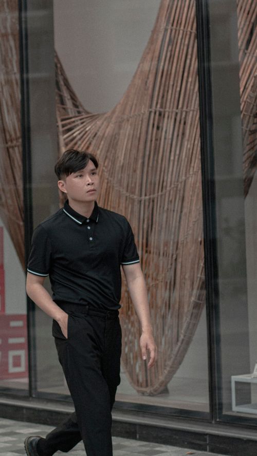Free Asian man in black attire walking along a sidewalk in urban setting. Stock Photo