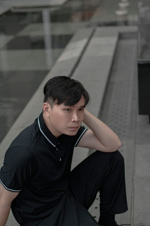 Free A young Asian man in a polo shirt sits thoughtfully in an urban environment, captured in a vertical shot. Stock Photo