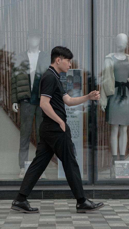 Free Man in black attire walks past a boutique window with mannequins on display. Stock Photo
