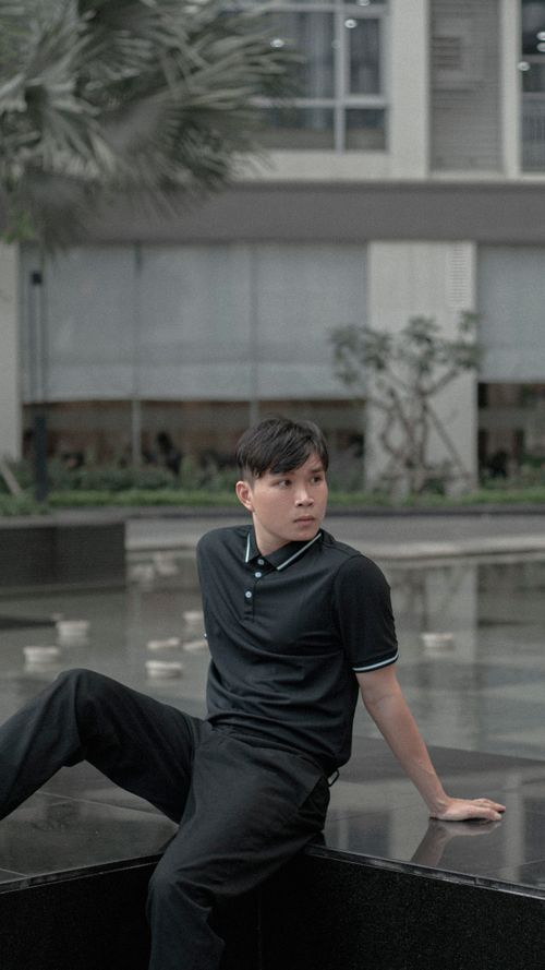 Free Asian man in black polo and pants relaxing by a modern building outdoors. Stock Photo