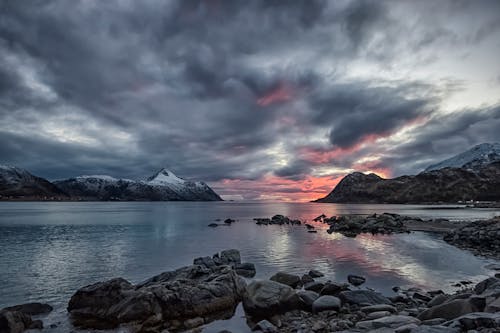 Rocky Shore With Mountain in Distance Under Gray Cloudy Sky