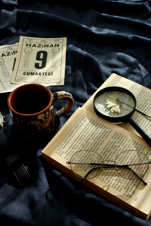 Free A nostalgic still life featuring a mug, open book, glasses, and magnifying glass on a dark cloth. Stock Photo