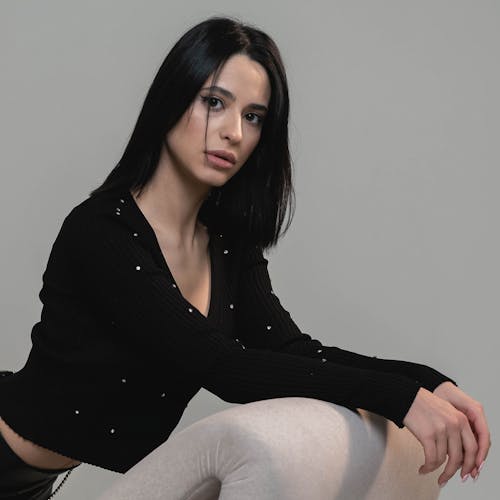 Woman in Black Long Sleeves Crop Top Leaning on a Couch while Seriously Looking at the Camera