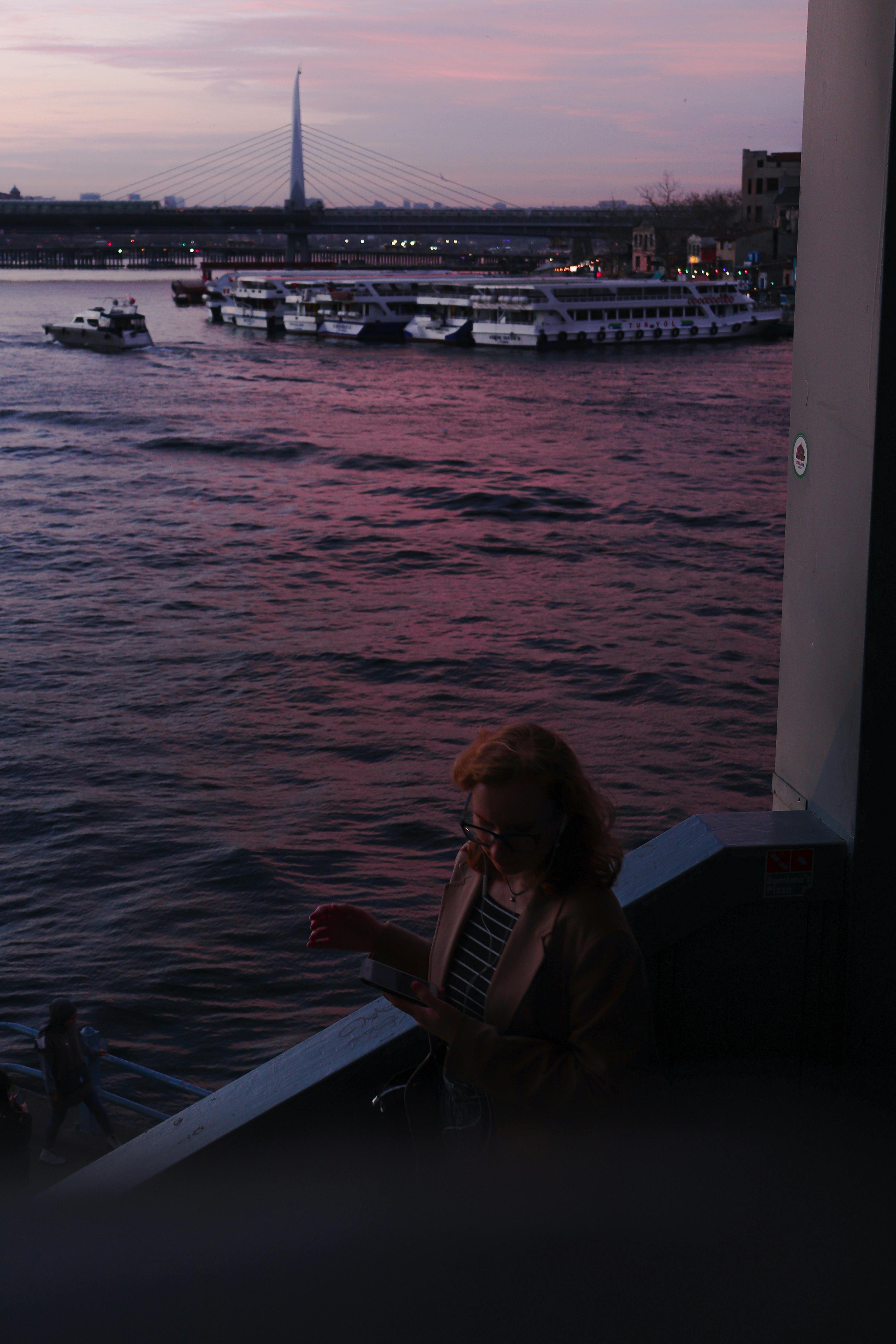 Peaceful twilight view over the river with a woman at the railing and passing boats.