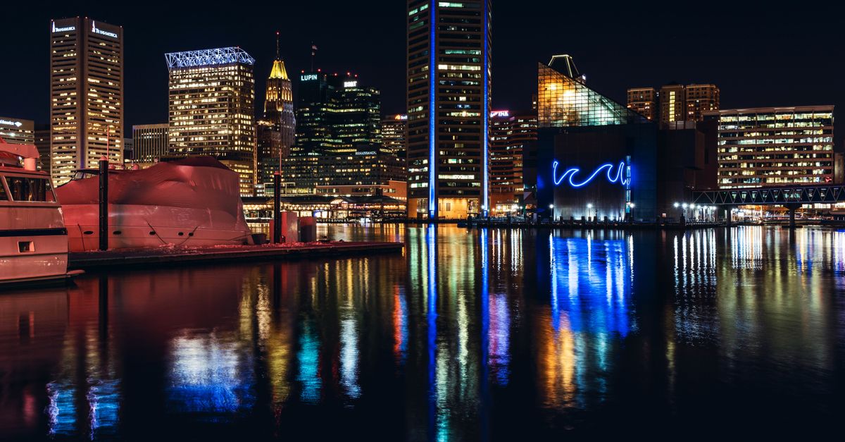 Vibrant Baltimore skyline at night with reflections on Inner Harbor water.