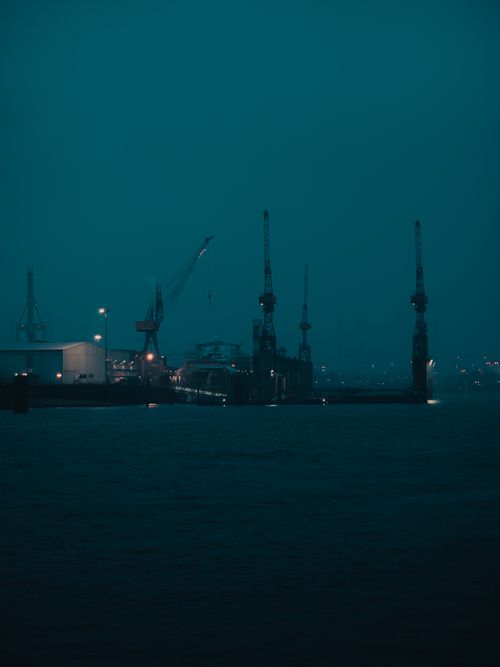 Free A dark and moody night scene at a harbor with silhouetted cranes and a calm sea. Stock Photo