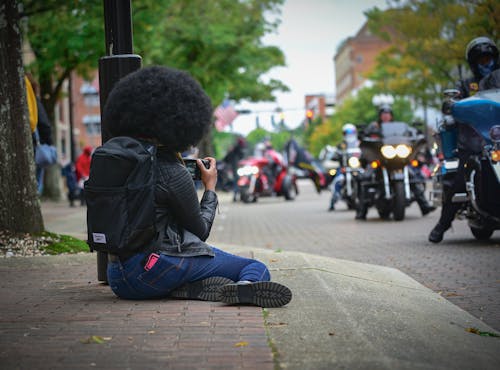 A Woman in Black Jacket and Blue Denim Jeans Sitting on Sidewalk