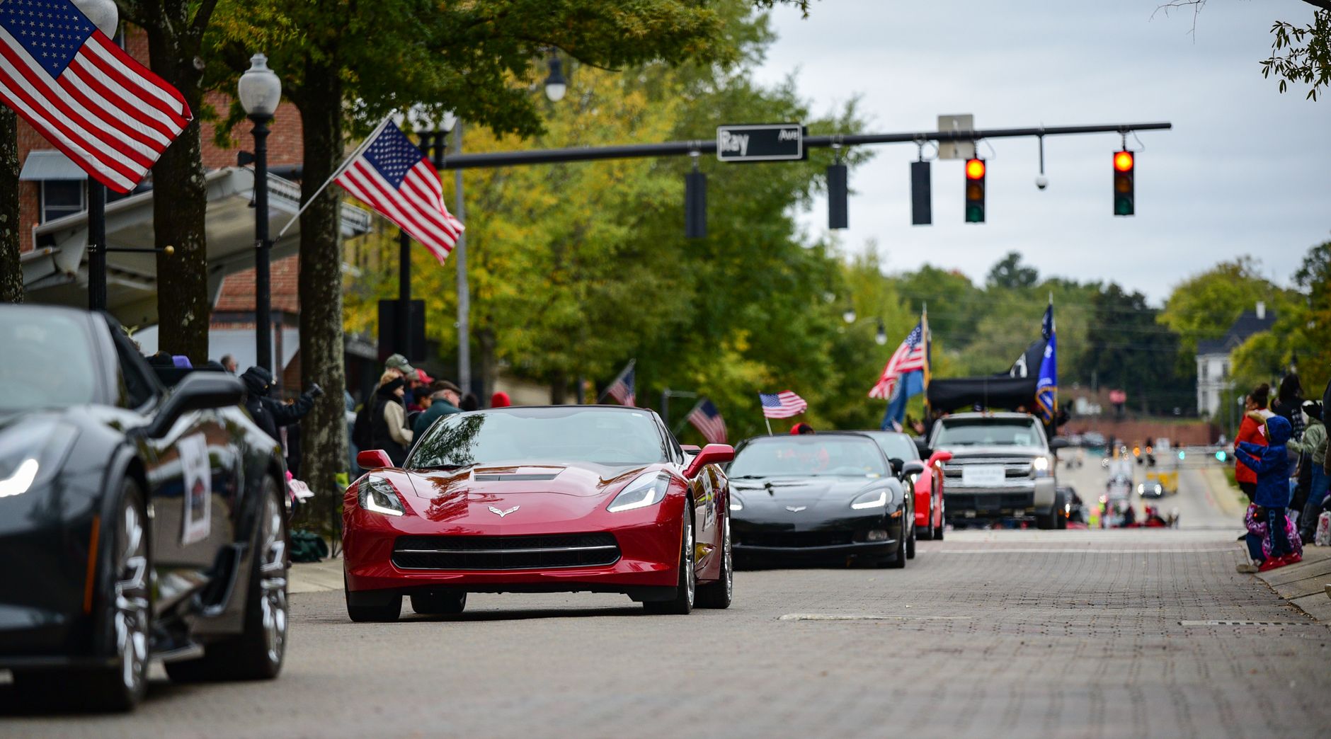 A vibrant parade in downtown Fayetteville, NC, featuring Corvettes and American flags.