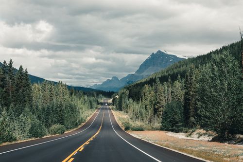 Free A picturesque road through a forested mountain landscape under a cloudy sky. Stock Photo