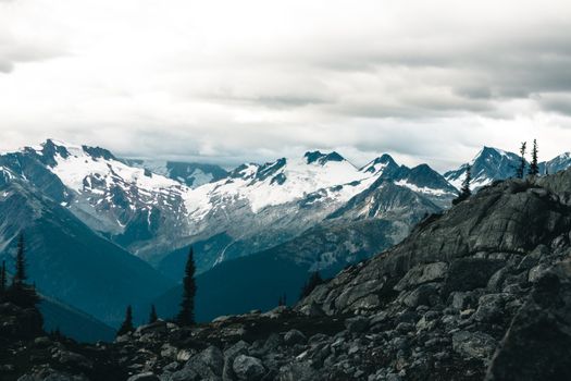 Breathtaking view of snow-covered Rocky Mountains with a dramatic cloudy sky backdrop.