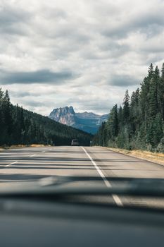 Stunning view of a Canadian highway with majestic mountains in the distance under a cloudy sky.
