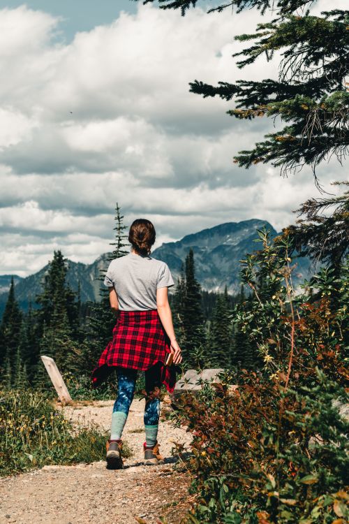 Free A woman hiking through a scenic mountain trail in Canada with lush greenery and cloudy skies. Stock Photo