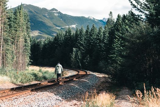 A solitary person walks on a railway track surrounded by lush pine trees and mountains in Canada.