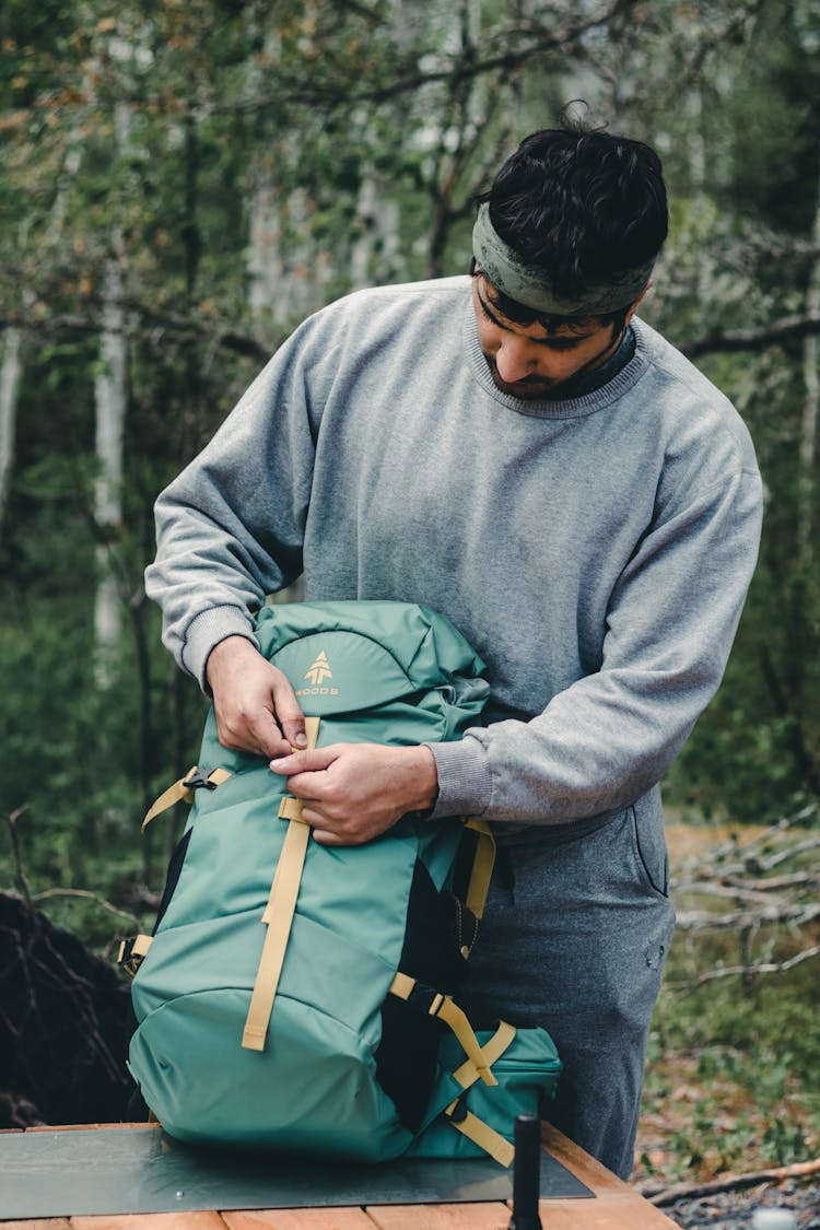 Man In Gray Sweater Closing The Backpack On A Wooden Table