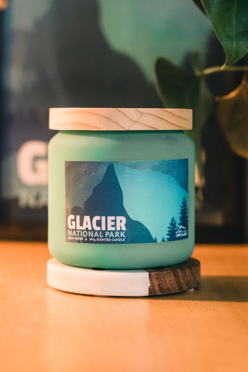 Free Eco-friendly Glacier National Park scented candle on table with soft lighting and plant accent. Stock Photo