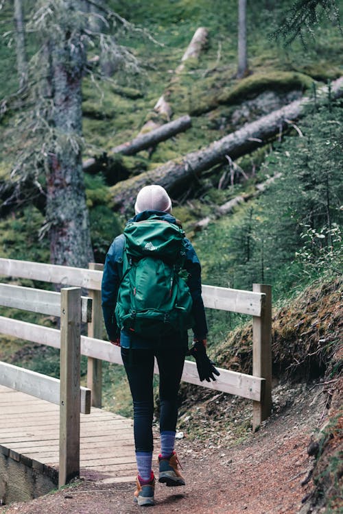 A Person Carrying Backpack Walking on a Wooden Bridge