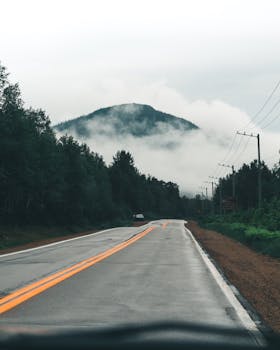 A picturesque road in Canada leading towards a misty, cloud-covered mountain peak.