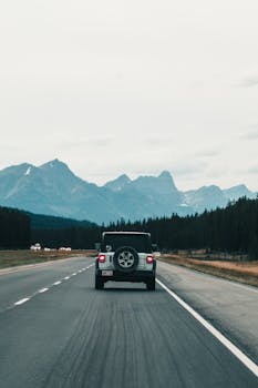 A jeep drives on an empty road towards the majestic Canadian Rockies.