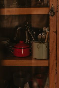 A cozy kitchen shelf featuring a red pot and utensils in a rustic wooden cabinet.