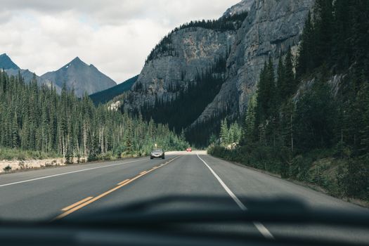 Scenic view of a quiet mountain road in Canada, surrounded by lush forests and towering peaks.