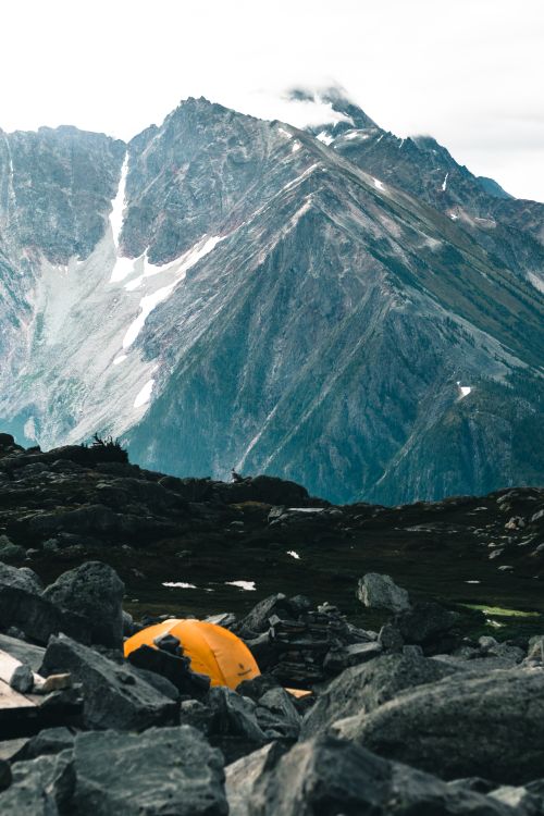 Free A breathtaking campsite nestled in the rocky Canadian mountains with a vibrant orange tent. Stock Photo