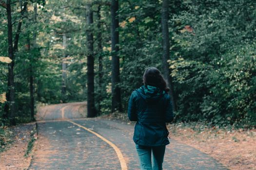 Rear view of a woman walking through a lush Canadian forest path during fall.