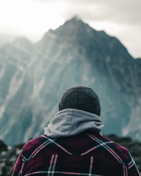 A person in a plaid jacket gazes at misty mountains in Canada, creating a serene atmosphere.