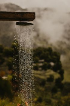 A serene outdoor shower with cascading water, set against a misty forest backdrop.