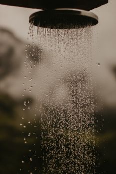 Close-up of water droplets falling from a shower head in an outdoor natural setting.