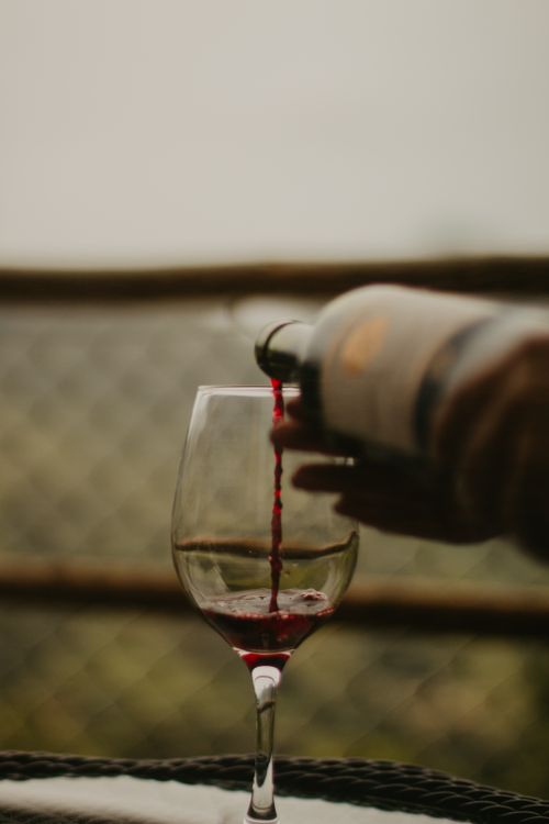 Free A close-up of red wine being elegantly poured into a clear glass outdoors. Stock Photo