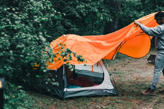 A man sets up a tent in a lush Canadian forest, perfect for summer camping adventures.