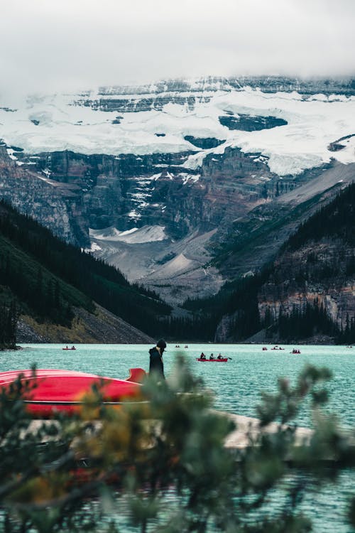 Person Standing on Red Boat on Lake Beside Mountains