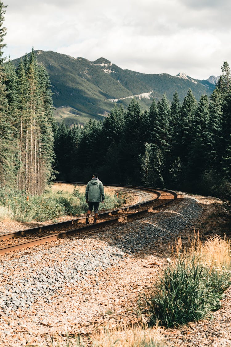 Man In Green Coat Standing On Train Rail In Mountains