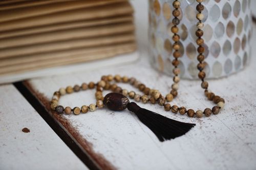 Free A close-up of a handmade beaded necklace with a tassel displayed on a rustic white wooden surface. Stock Photo