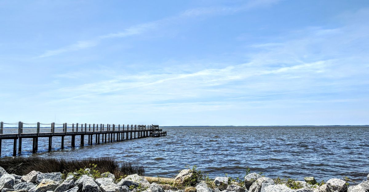 Peaceful oceanfront view with a long pier and rocky shore in Kinnakeet, NC.