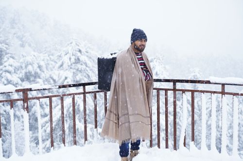 Free Man standing on snowy balcony with blanket and backpack in winter setting. Stock Photo