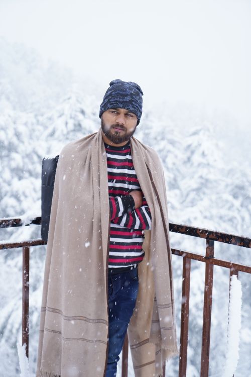 Free A man wrapped in a blanket stands on a snowy balcony, showcasing a serene winter scene. Stock Photo