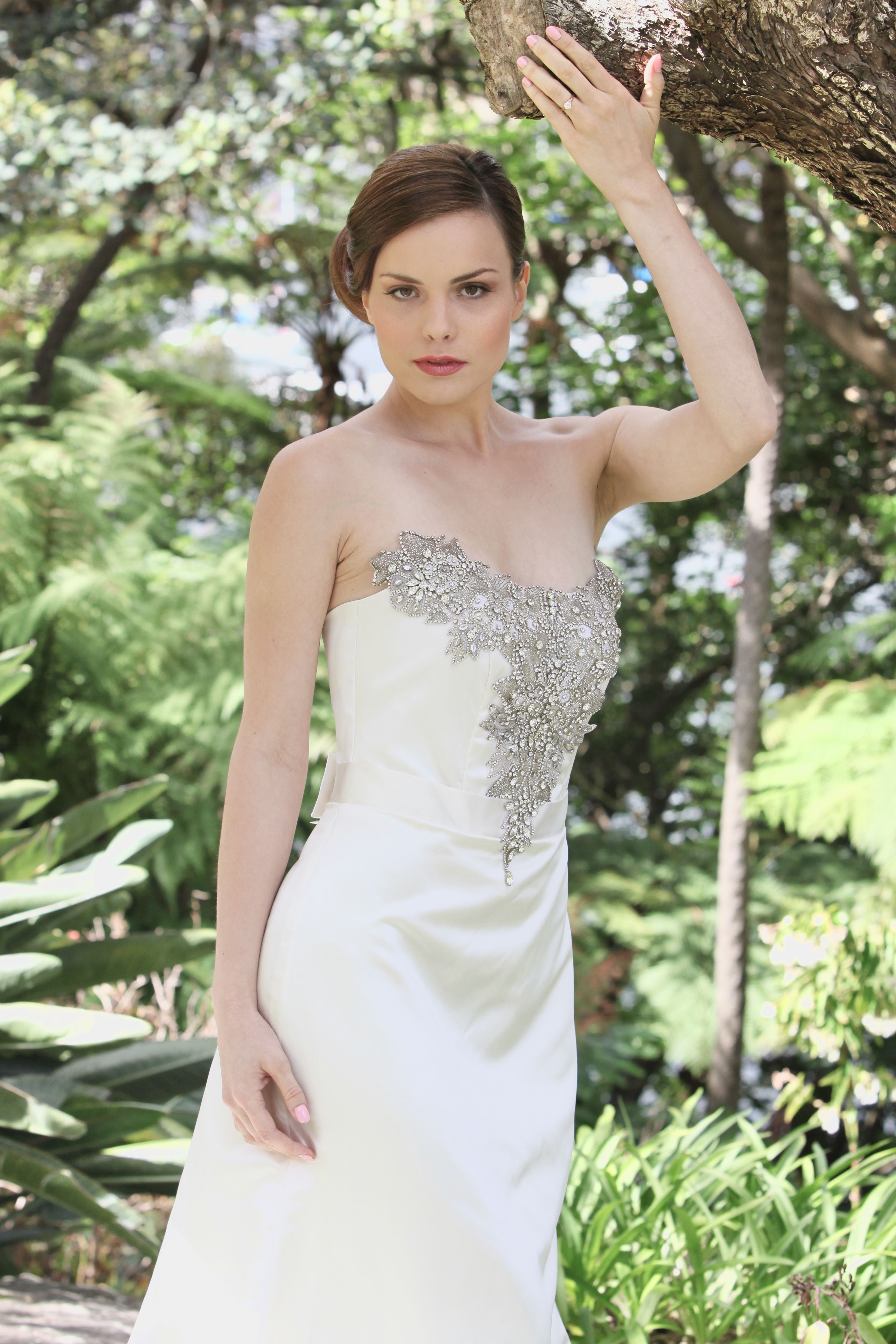 Stunning bride in a strapless wedding dress poses gracefully in a verdant garden setting.